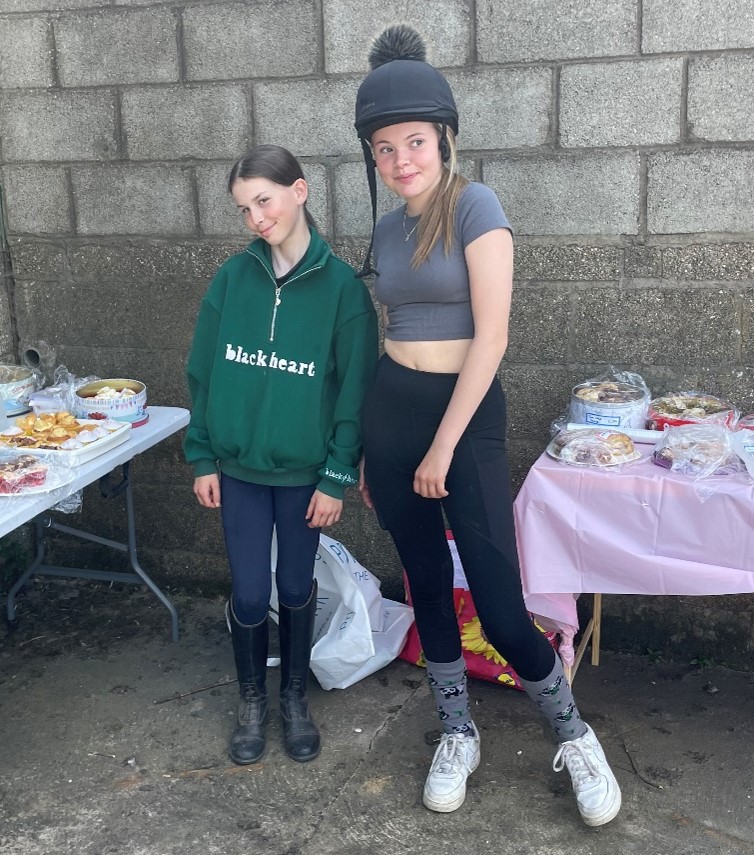 2 students with tables of cakes to sell to raise funds for Cancer Research