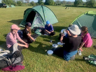 group of students sitting outside tents in a field