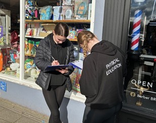 students outside shop writing on clipboards
