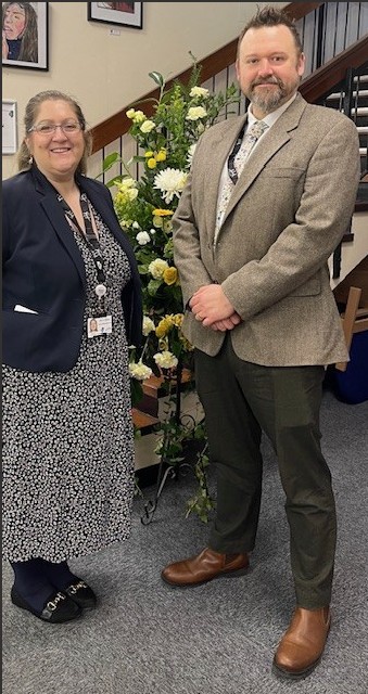 2 teachers stood by a flower arrangement