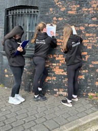 students writing on clipboards leaning against a wall